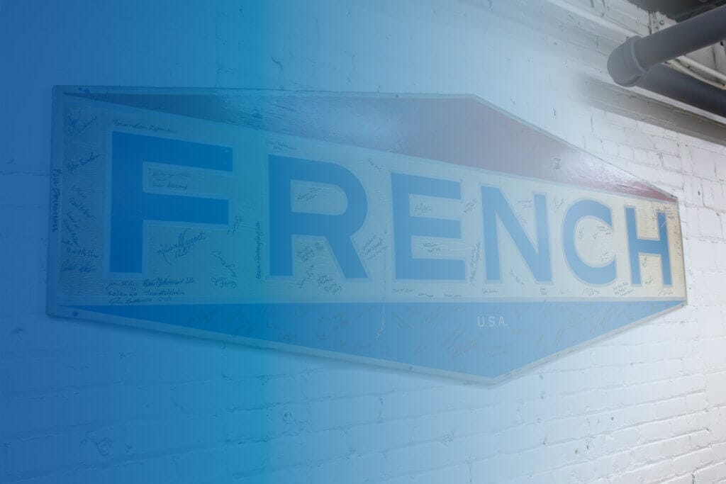 Vintage French Oil logo signed by employees and guests during the company’s 125th anniversary celebration, displayed on a white brick wall at French Oil Mill Machinery Company’s headquarters.